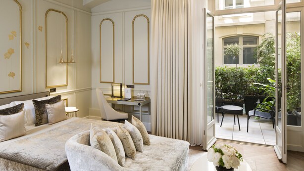 Un dormitorio lujoso con una cama grande, un sofá, un escritorio y vistas a un patio exterior con plantas y mobiliario.