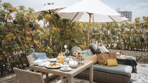 Un patio al aire libre con mobiliario de mimbre, una mesa de comedor con platos y bebidas, y sombrillas que dan sombra.
