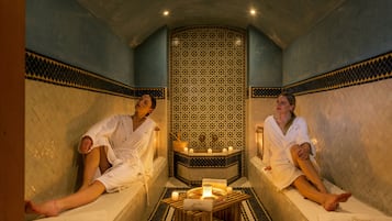 Guests can unwind in a serene spa setting with tile-adorned walls and a central column, surrounded by candles and a tranquil atmosphere.