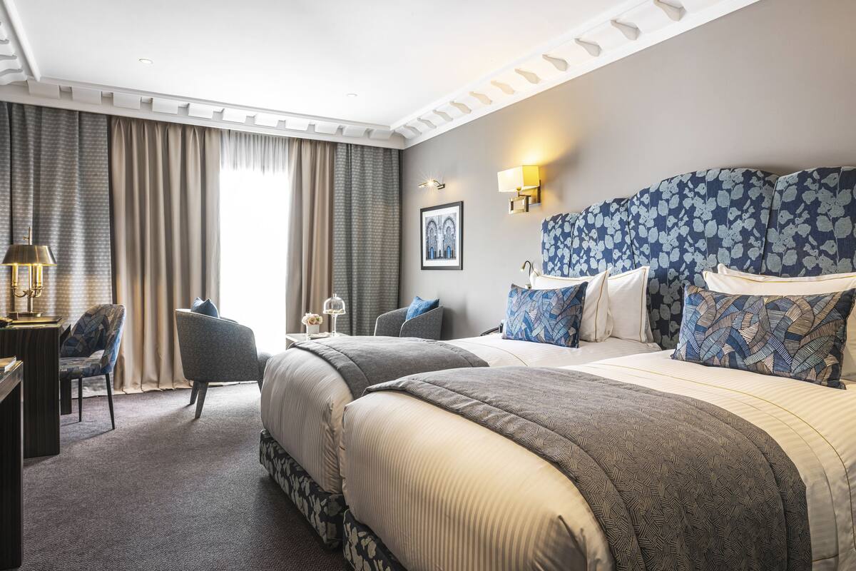 A hotel room with two beds, a desk, a chair, and a large window with curtains.