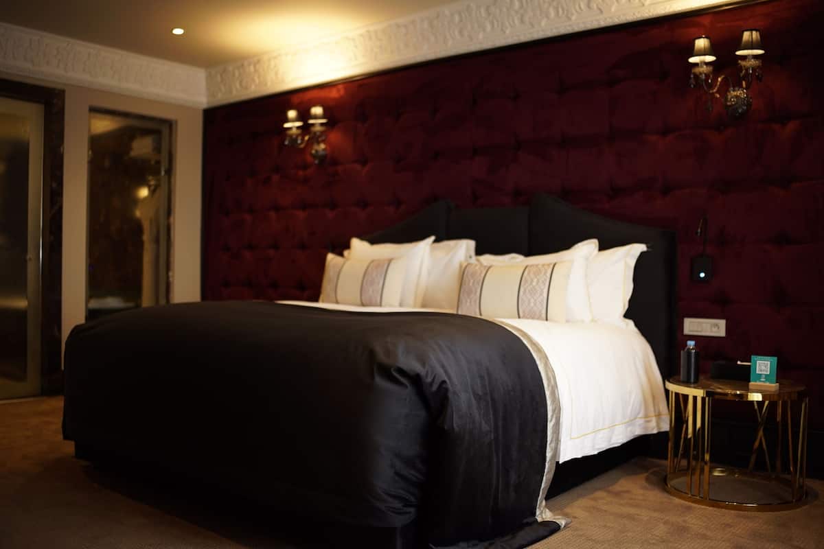 A large bed with a dark headboard, white bedding, and two wall sconces.