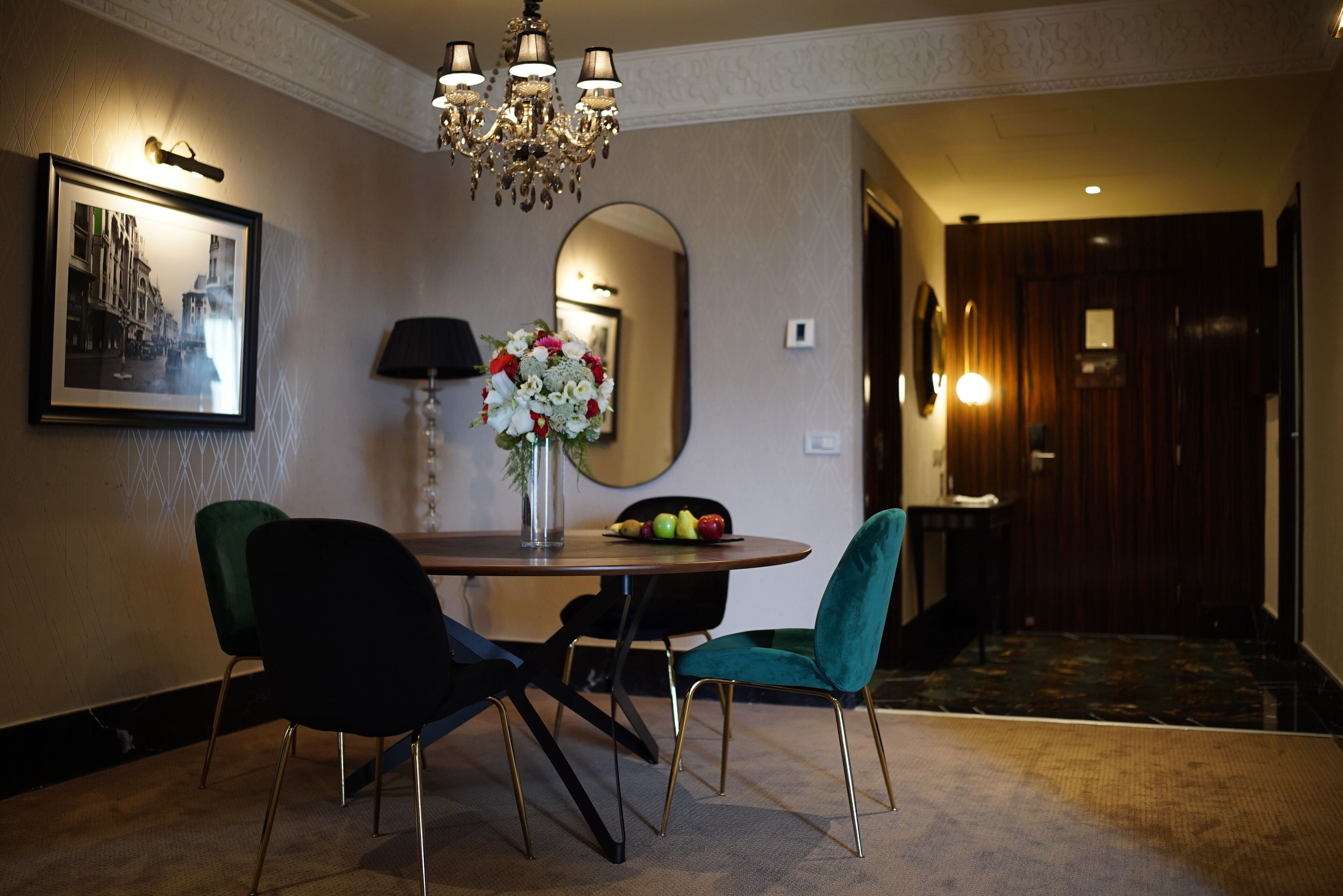 Un'area pranzo con un tavolo rotondo, due sedie, un vaso con fiori, un quadro incorniciato e un lampadario.