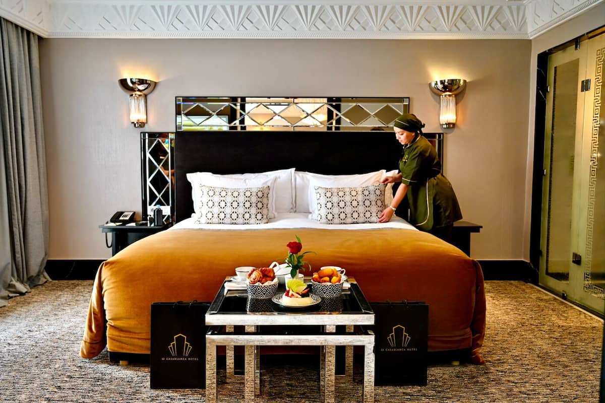 A hotel room with a large bed, a bedside table with a tray of breakfast, a nightstand with a phone, and a wall-mounted light fixture.