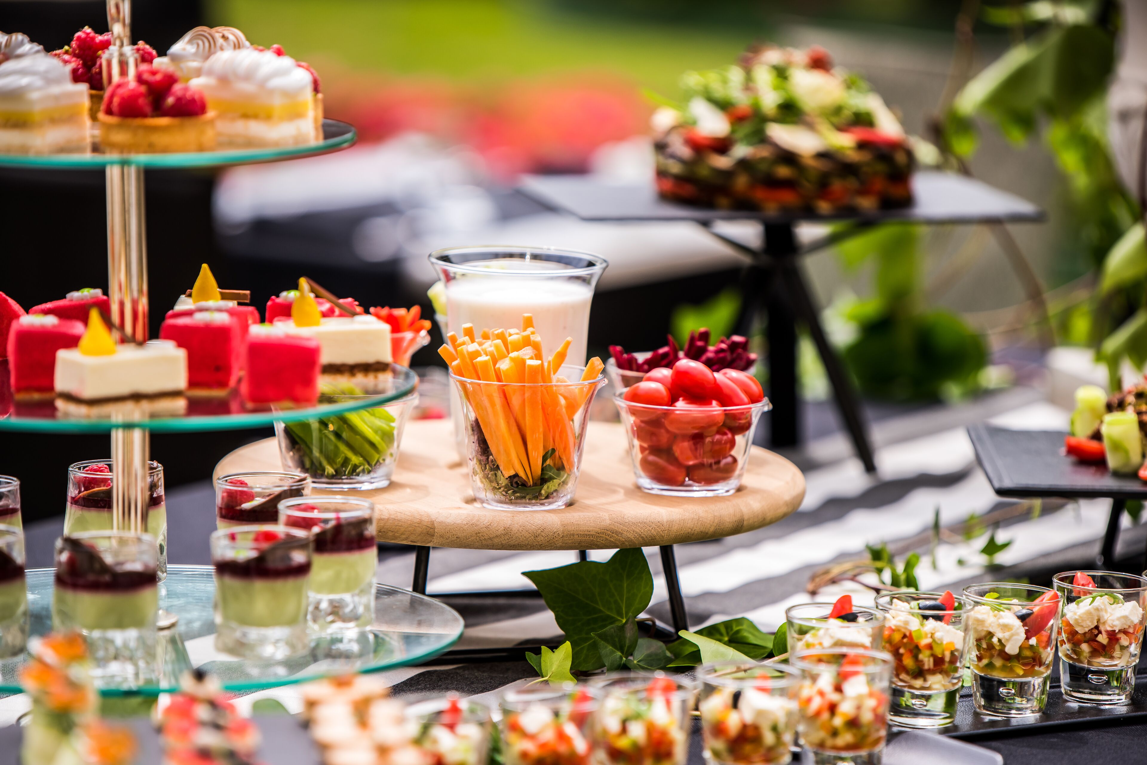 Eine Auswahl an Desserts und Getränken auf einem Buffet, darunter mehrschichtige Kuchen, Obst und ein Glas mit Karottensticks.