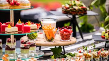 Eine Auswahl an Desserts und Getränken auf einem Buffet, darunter mehrschichtige Kuchen, Obst und ein Glas mit Karottensticks.