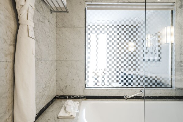 A bathroom with a checkered glass shower door, a white bathtub, and a towel on the floor. - Le Casablanca Hotel (Casablanca)