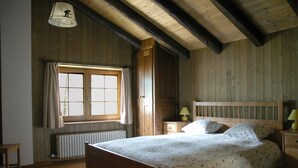 A bedroom with a wooden bed, a nightstand, a lamp, a window with curtains, and a radiator. - Bed & Breakfast Della Miniera (Cogne)