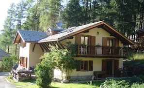 Uma casa de dois andares com varanda, rodeada por vegetação e árvores.