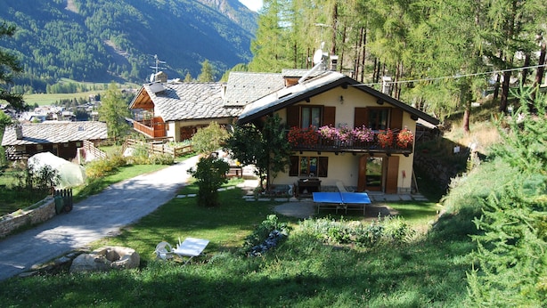A mountain lodge with a wooden deck, a ping pong table, and a stone wall. - Bed & Breakfast Della Miniera (Cogne)