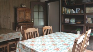 A dining area with a table set for four, wooden chairs, a cabinet, and a bookshelf with books and a small plant. - Bed & Breakfast Della Miniera (Cogne)