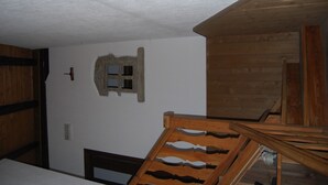 A room with a wooden ceiling, a stone wall with a small window, and a wooden chair. - Bed & Breakfast Della Miniera (Cogne)