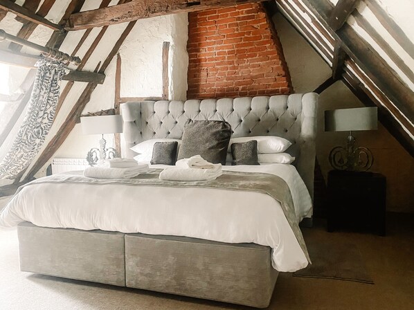 A bedroom with a tufted headboard, a brick wall, and a sloped ceiling. - The Kings Head Bawburgh (Norwich)