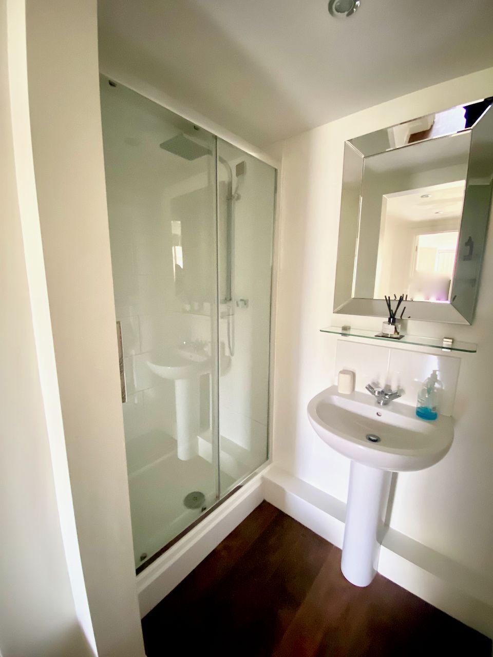 A bathroom with a glass shower enclosure, a pedestal sink, and a mirror above the sink.