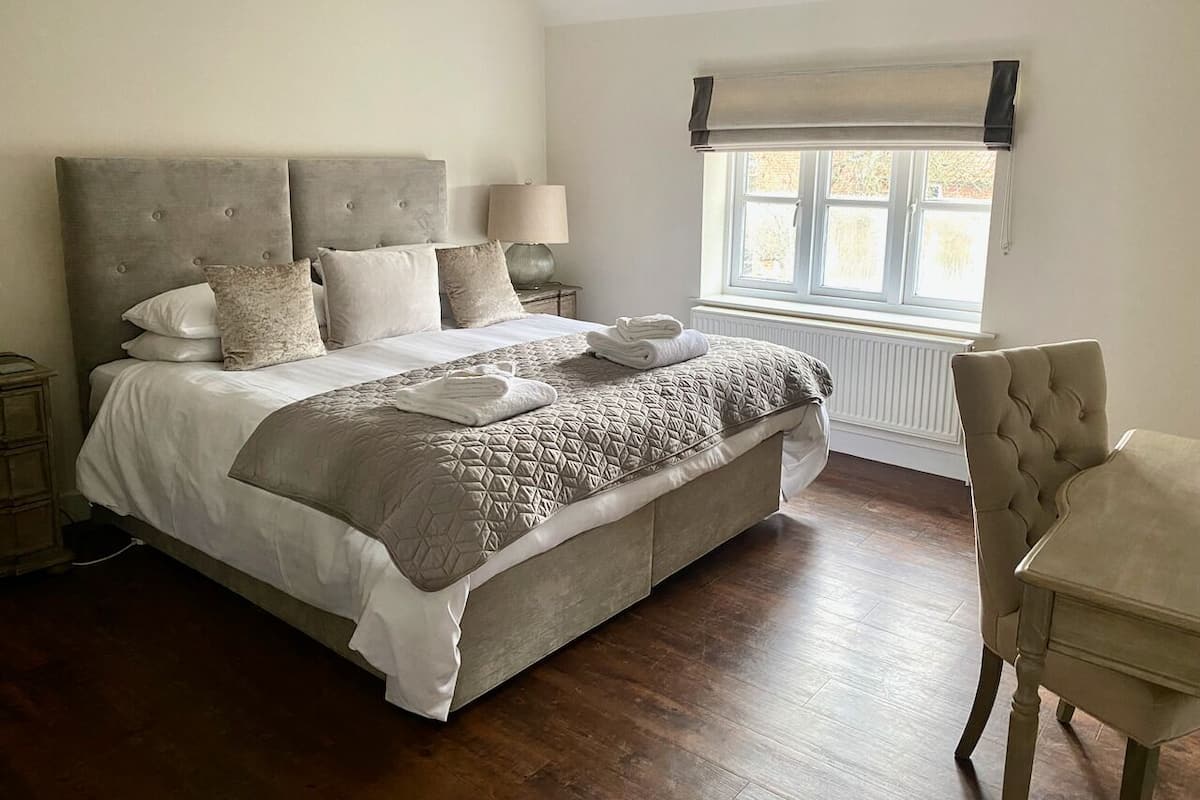 A bedroom with a large bed, a bedside table, a lamp, a chair, and a window with a view.