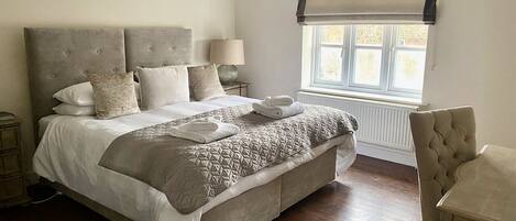 A bedroom with a large bed, a bedside table, a lamp, a chair, and a window with a view.