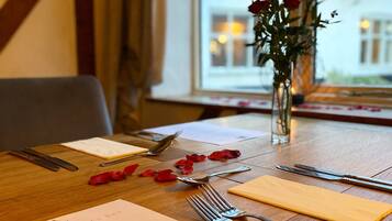 A dining table set with cutlery, a menu, and rose petals.