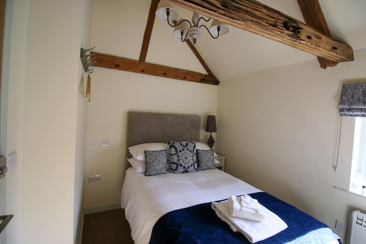 A bedroom with a bed, a nightstand, a lamp, and a window with a curtain.
