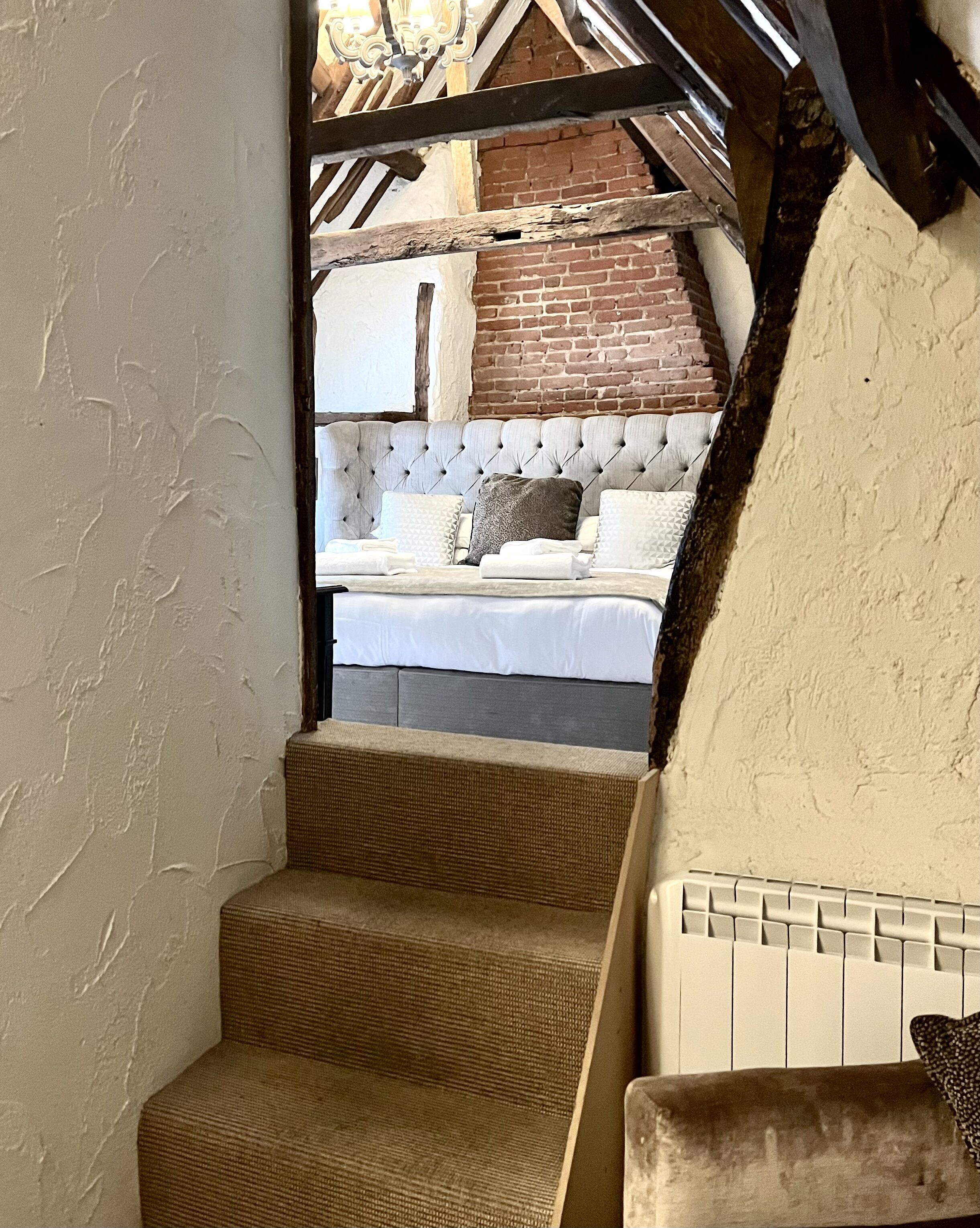 Un escalier menant à une chambre à coucher dotée d’une tête de lit capitonnée et d’un mur en briques.