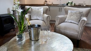 A living room with a round table, two armchairs, a fireplace, and a kitchen in the background. - The Kings Head Bawburgh (Norwich)