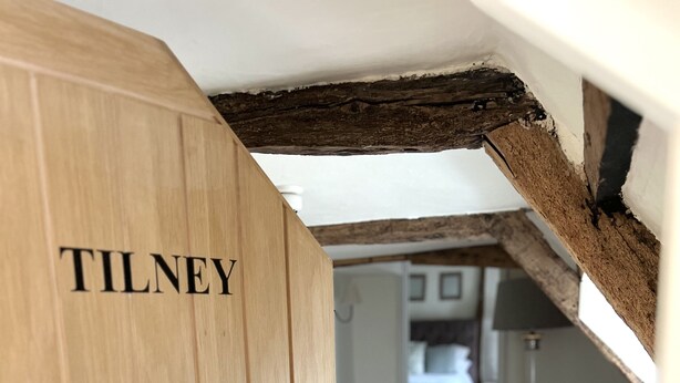A wooden door with the name "TILNEY" on it, leading to a room with a white bathtub and a grey sofa. - The Kings Head Bawburgh (Norwich)