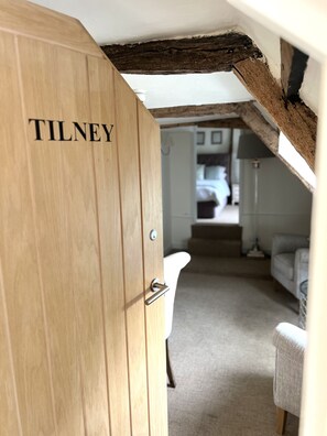 Una puerta de madera con el nombre "TILNEY" grabado, que da a un cuarto con una bañera blanca y un sofá gris.