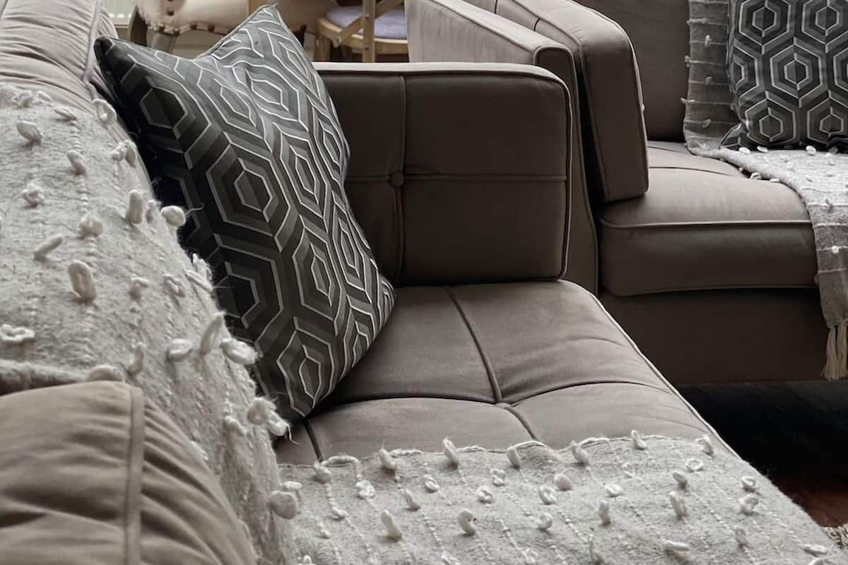 A cozy living room with a sectional sofa, patterned throw pillows, and a wooden dining table.