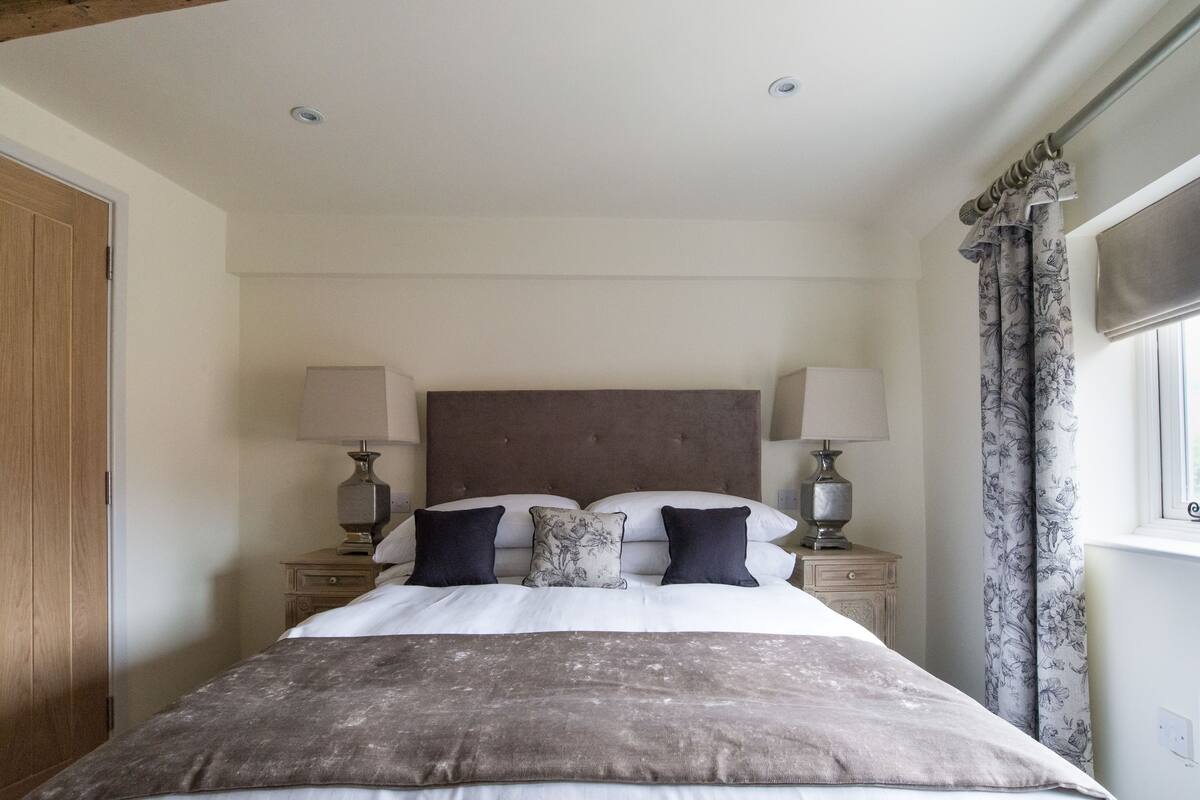 A bedroom with a large bed, two bedside tables with lamps, a wooden wardrobe, and a window with curtains.