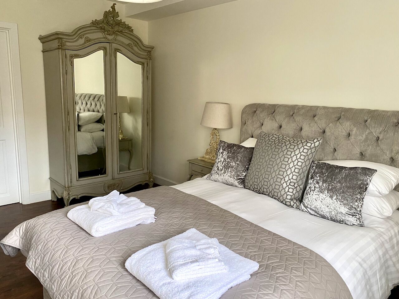 A neatly made bed with a large mirror and a lamp beside it.