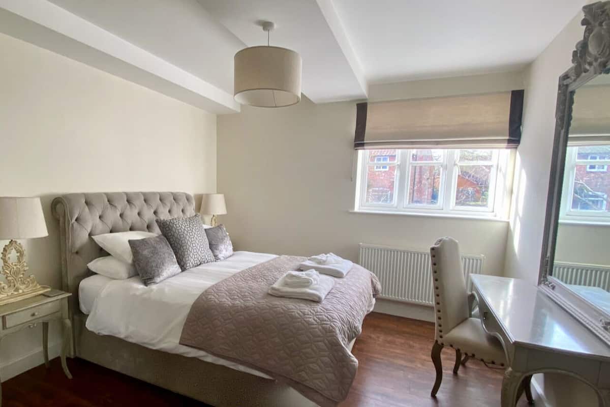 A neatly made bed with a headboard, a bedside table with a lamp, and a chair.
