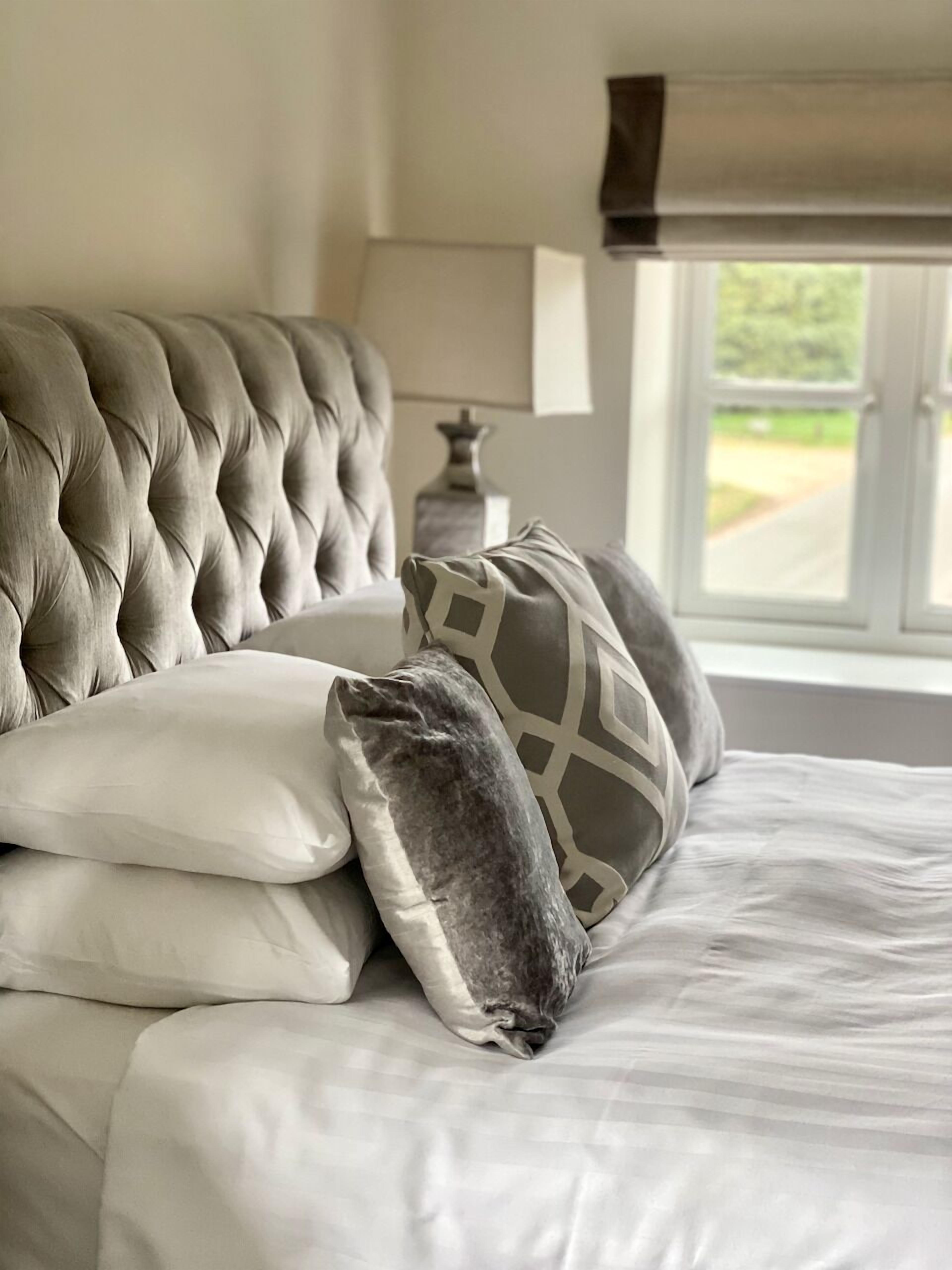 A bed with a tufted headboard, white bedding, and two pillows with geometric patterns.