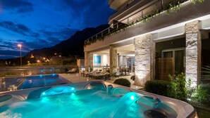 Un área de jacuzzi exterior de lujo con fachada de piedra y un balcón con vistas a un paisaje montañoso.