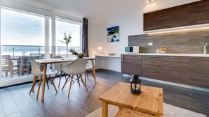 Una cocina moderna con armarios de madera oscura, encimera blanca y un ventanal con vistas al mar.