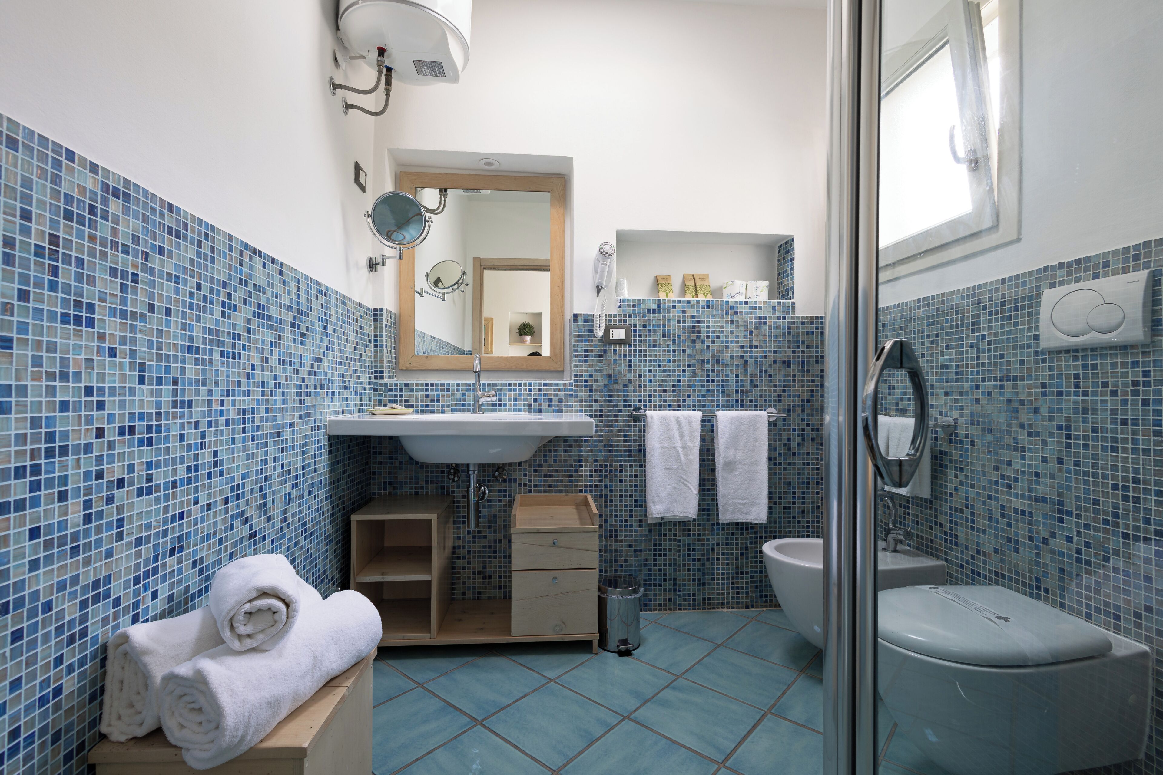Baño con lavamanos, espejo, toallero y zona de ducha.