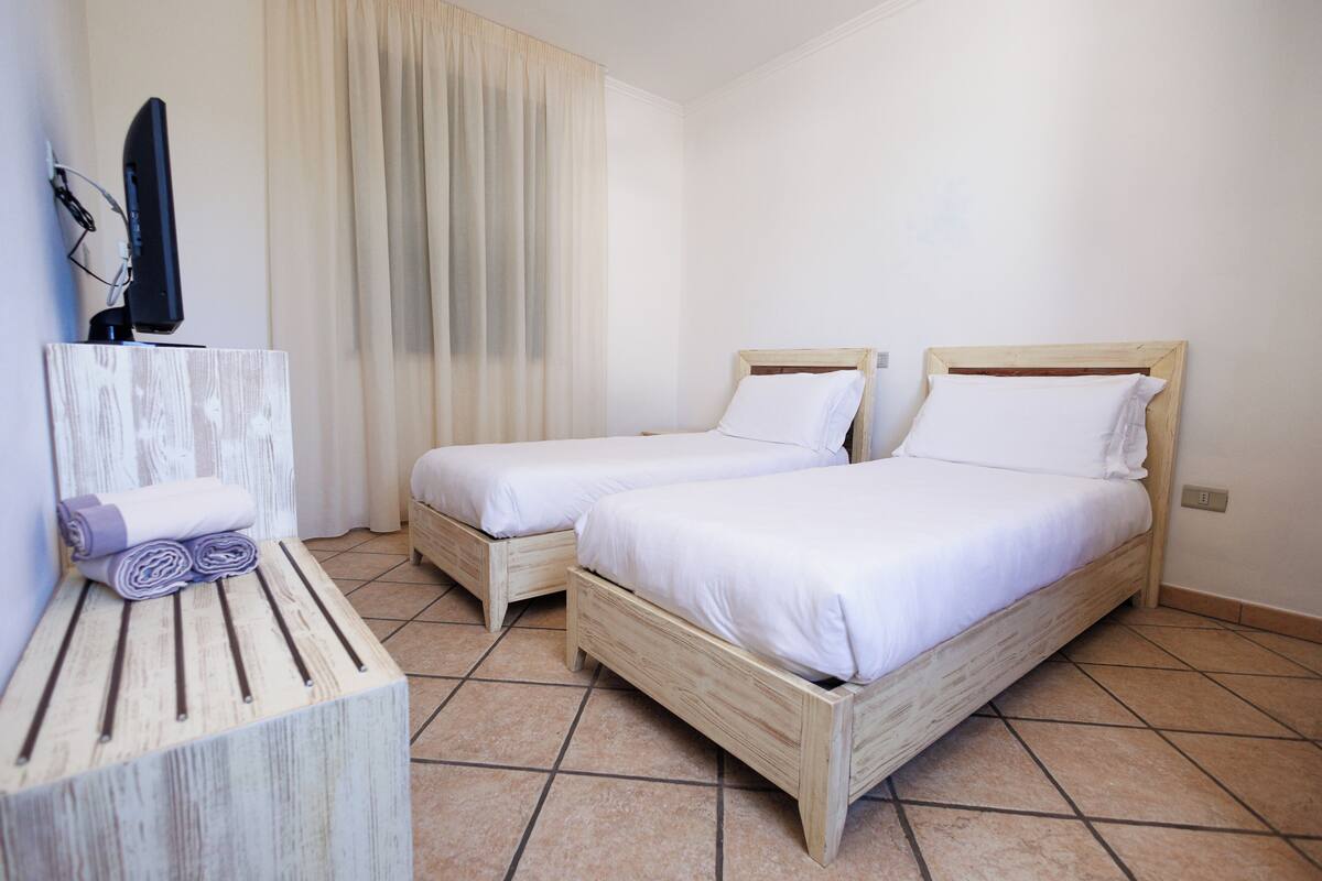 Una habitación de hotel con dos camas de madera, un televisor sobre un mueble de madera y una ventana con cortinas.