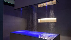Ein modernes Badezimmer mit einem rechteckigen Waschbecken, einer integrierten, blau beleuchteten Wasserfall-Dusche und einem beleuchteten Spiegel über dem Waschbecken.