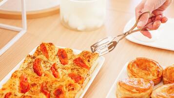 A hand holding a pair of scissors over a rectangular dish with food items, a white plate with pastries, and a candle in the background.