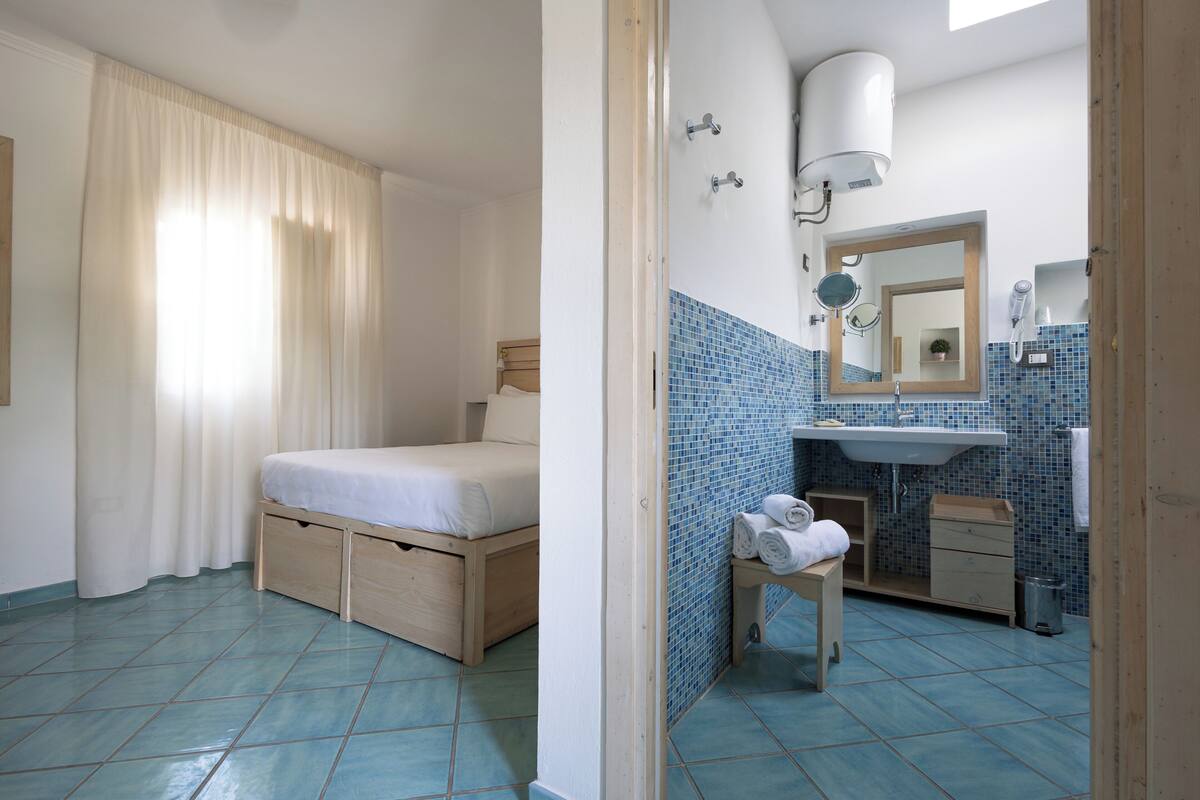 Un dormitorio con cama, mesita de noche y baño equipado con lavabo, espejo y toallero.
