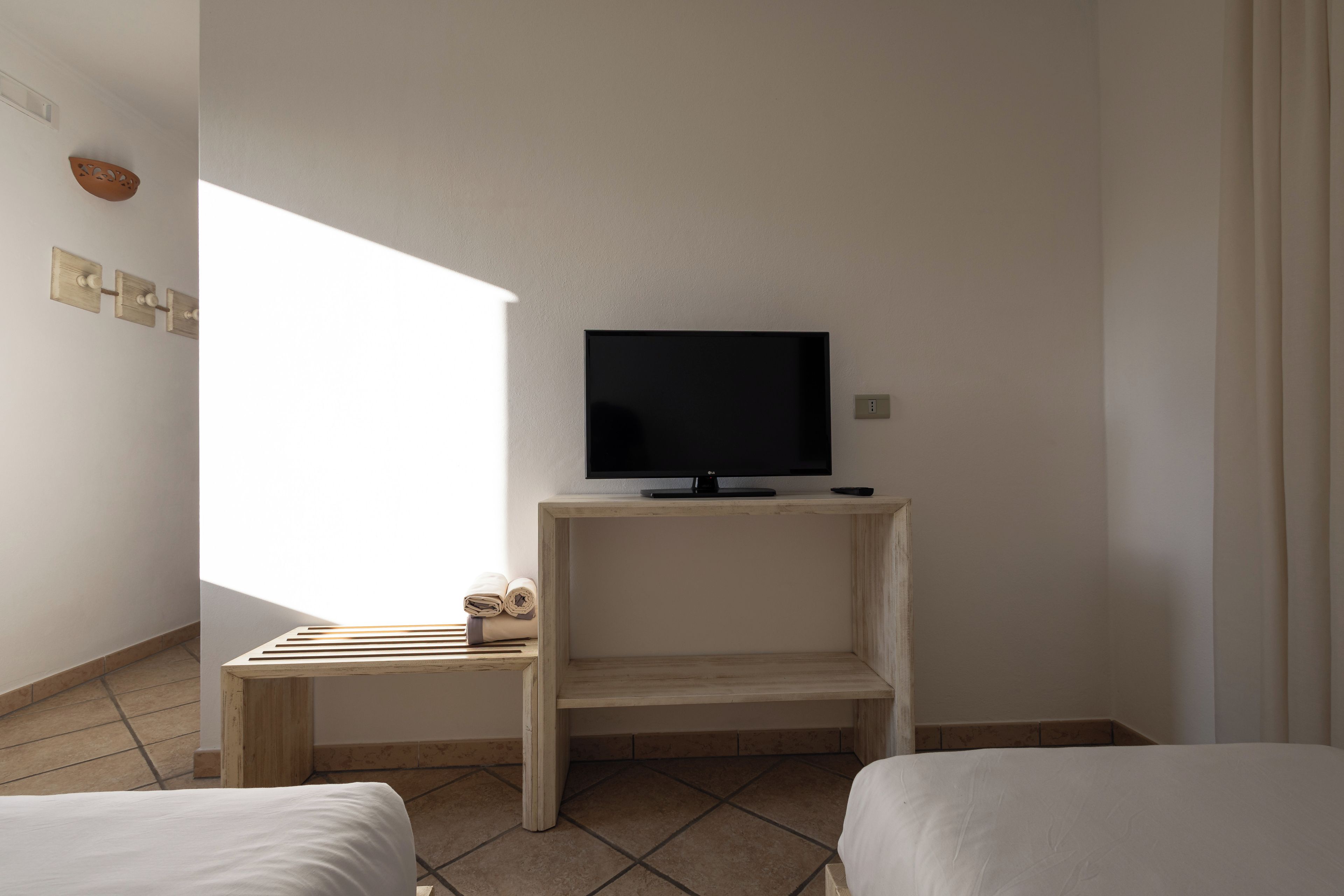 Quarto de hotel com televisão sobre um suporte de madeira, uma mesinha com toalhas e duas camas.