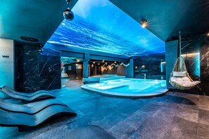 Un área de spa moderna con un jacuzzi grande, una camilla de masaje y una silla colgante.