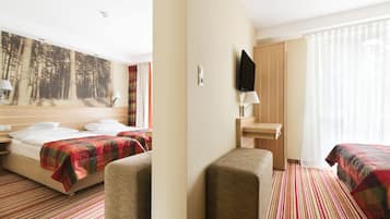 Habitación de hotel con dos camas, un mural grande de un bosque, un escritorio con una silla y una ventana con cortinas translúcidas.