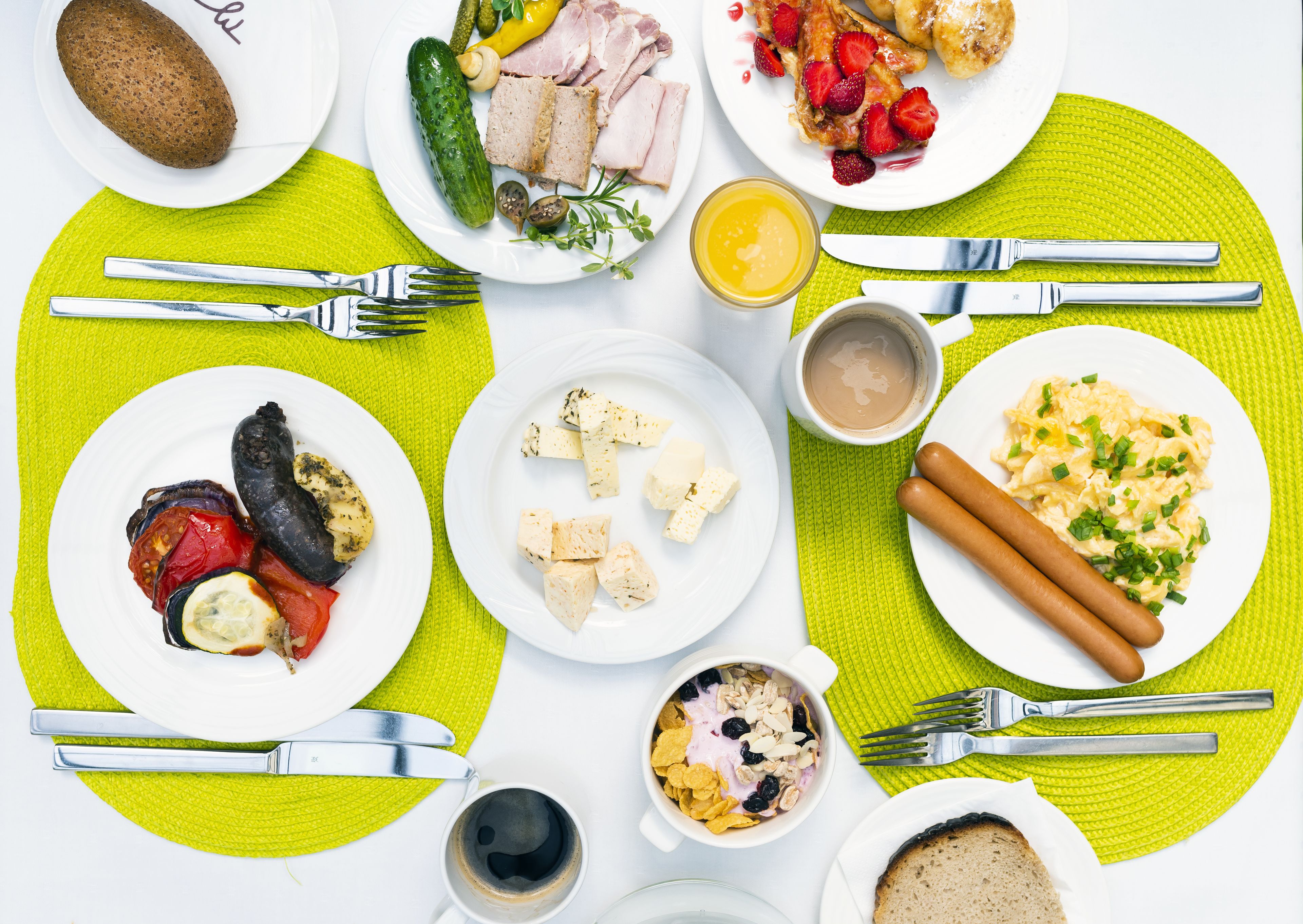 Een ontbijttafel met borden eten, bestek en een groene placemat.