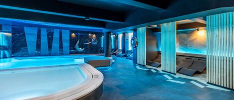 A modern spa area with a large hot tub, seating areas, and a wooden wall with vertical slats.