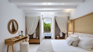 A bedroom with a large bed, a wooden desk, a round mirror, and a window with curtains. - Amalgam Homes Paros Beachfront Villa (Paros)