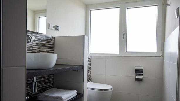 Une salle de bain moderne avec des toilettes blanches, un grand miroir et une fenêtre.