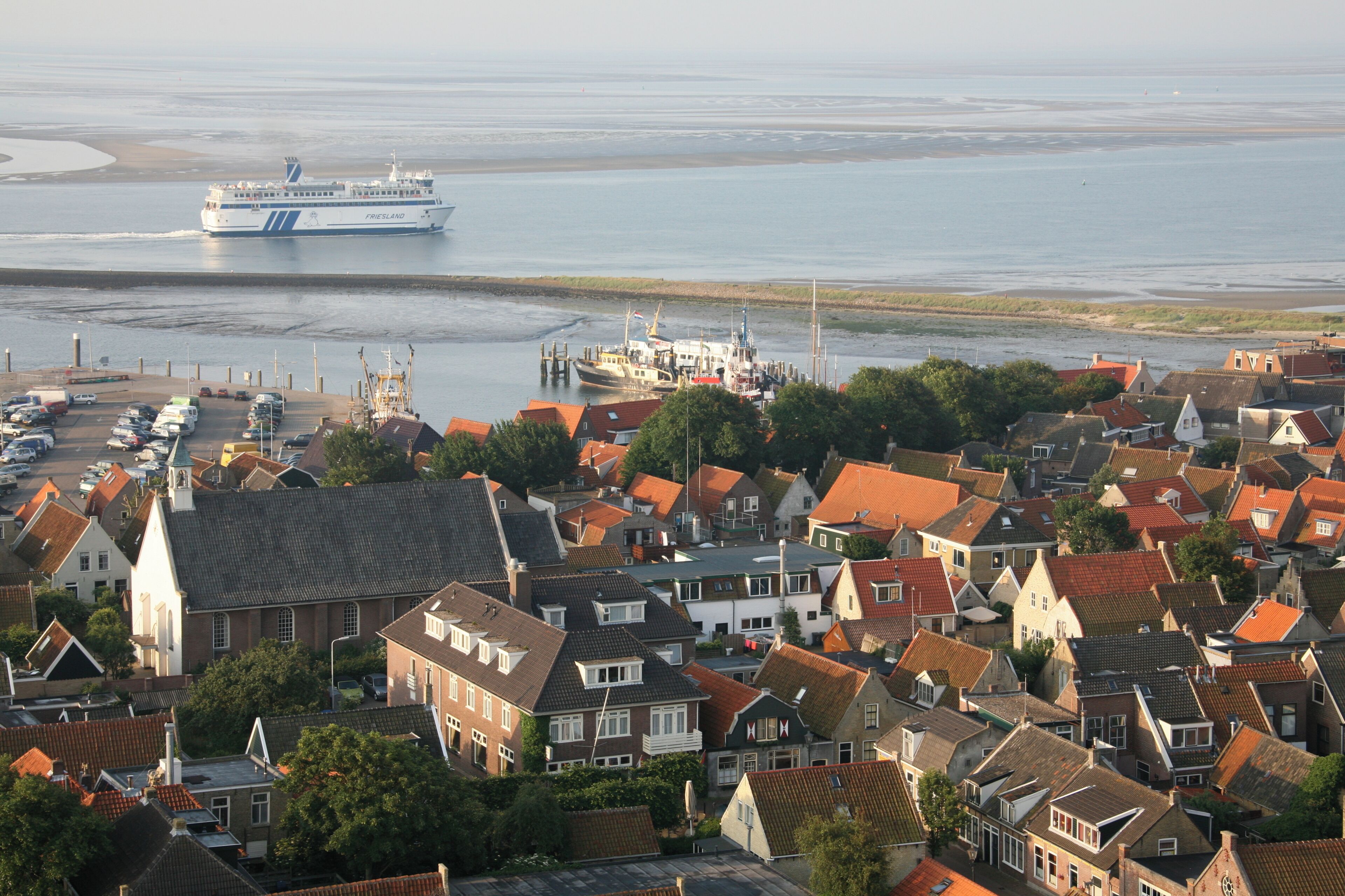 A coastal town with traditional architecture, a ferry dock, and a large ferry in the background.