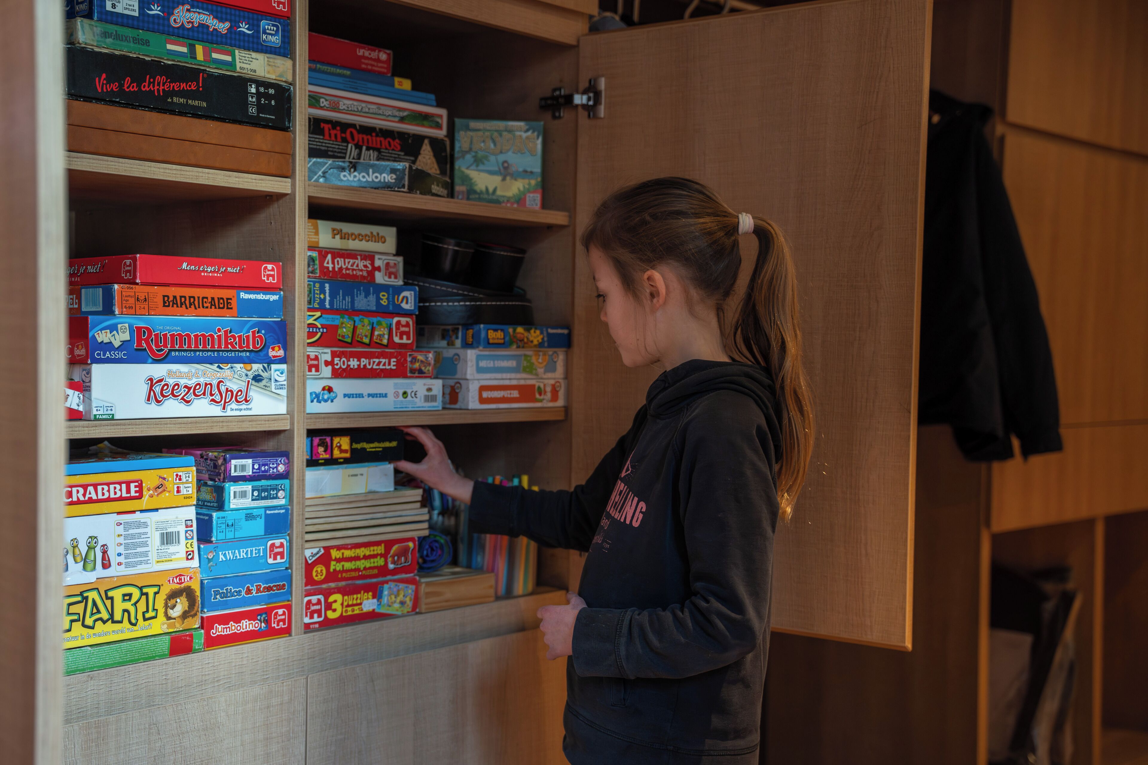 A person organizing board games on shelves in a room with wooden cabinets.