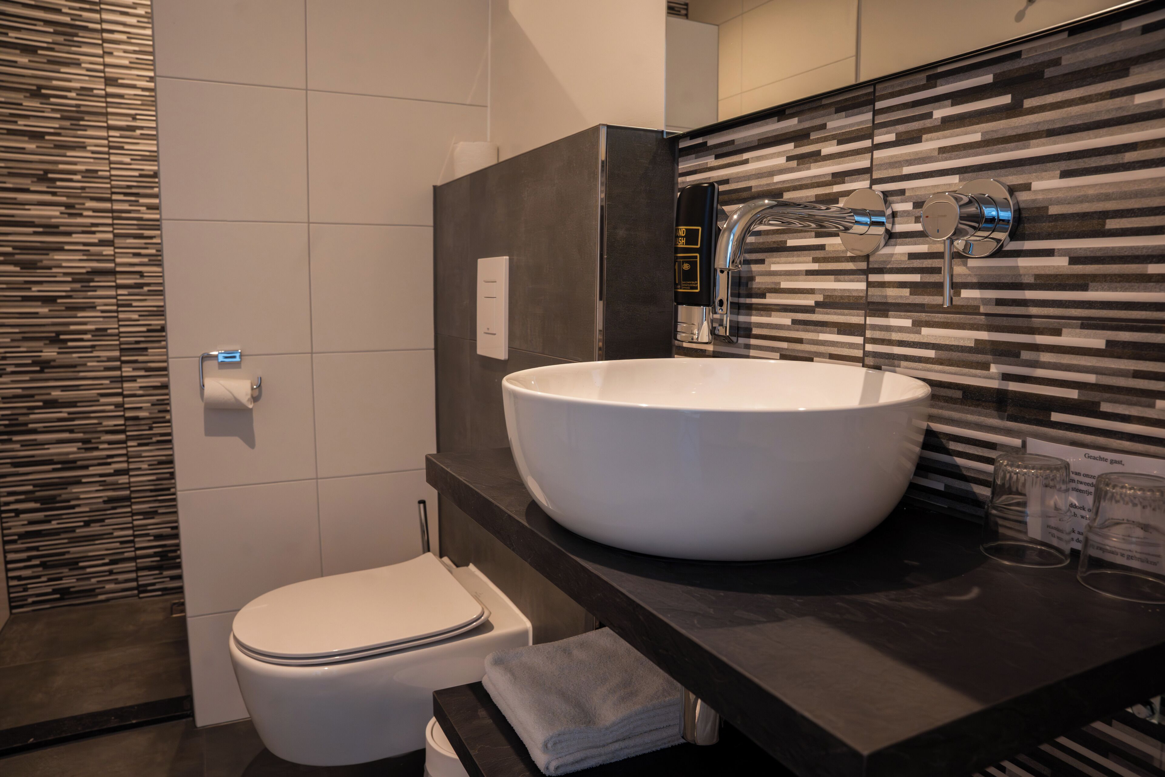 Un baño moderno con inodoro blanco, un lavamanos grande de color blanco y una encimera negra.