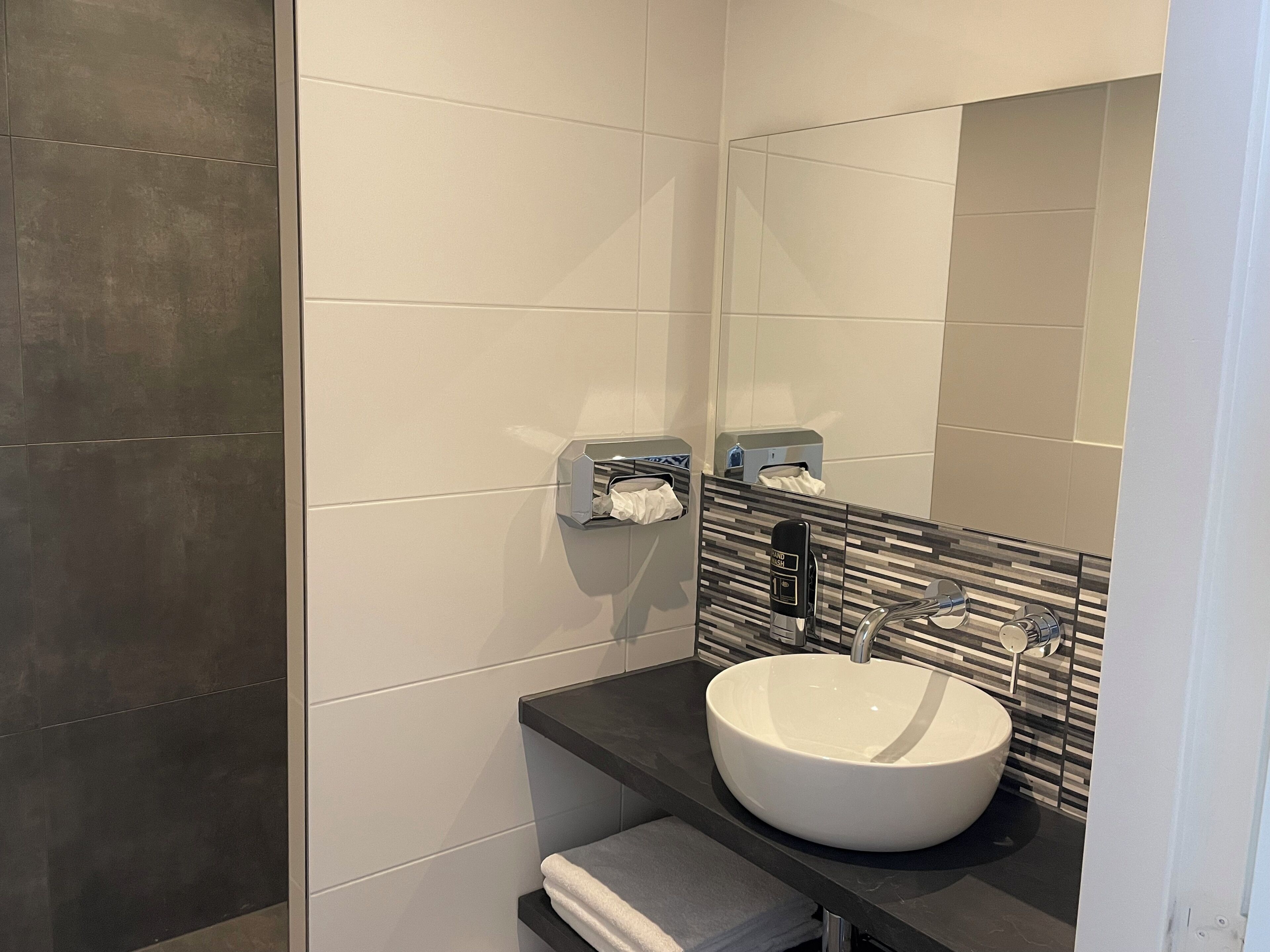 A modern bathroom with a large mirror, a white sink, and a towel rack.