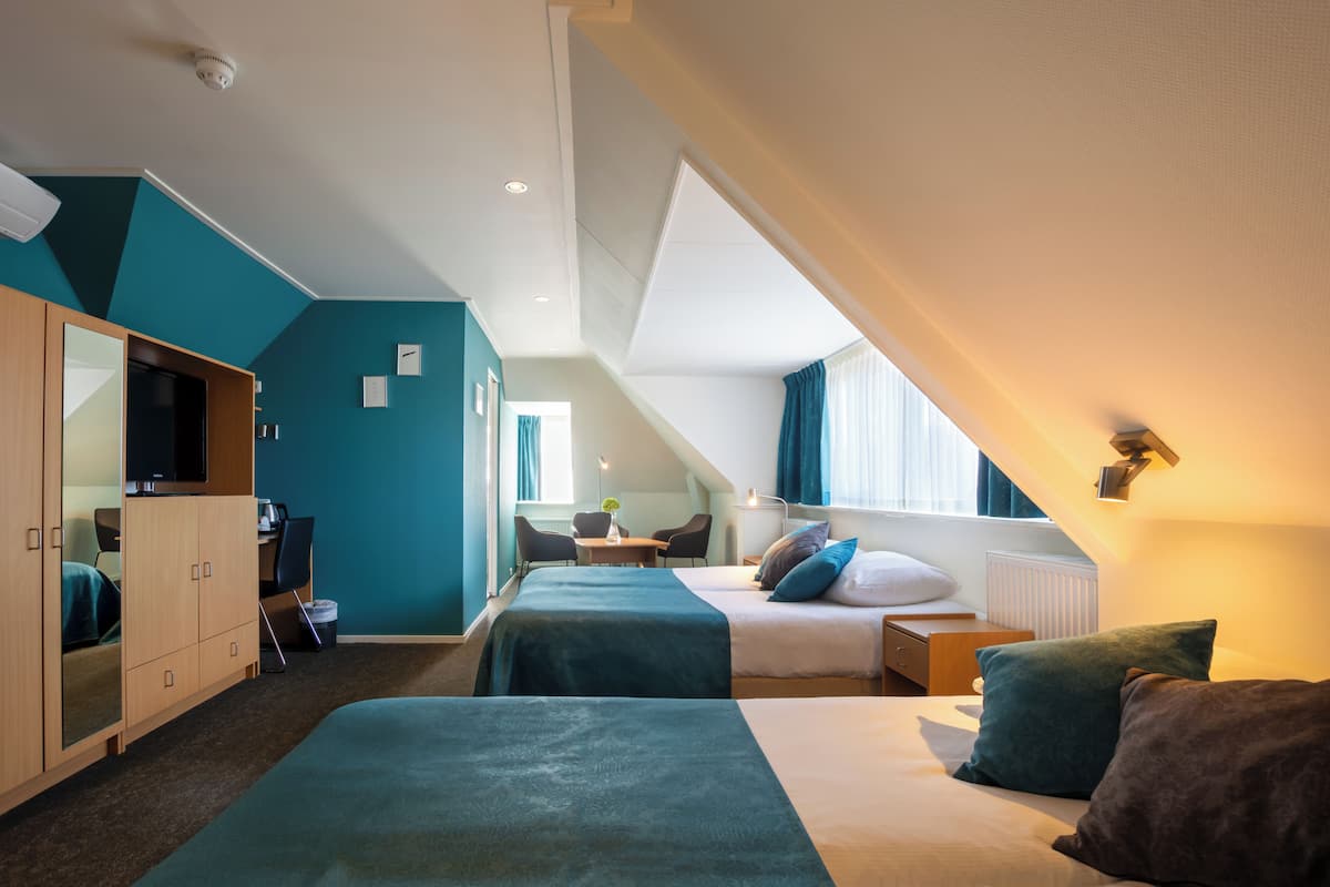 Een hotelkamer met twee bedden, een bureau, een stoel, een kledingkast en een raam met gordijnen.