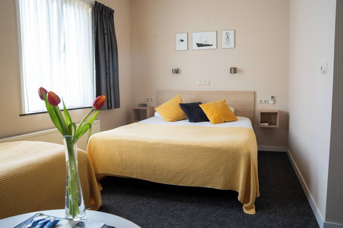 Een hotelkamer met een bed, nachtkastjes, een vaas met bloemen en kunst aan de muur.